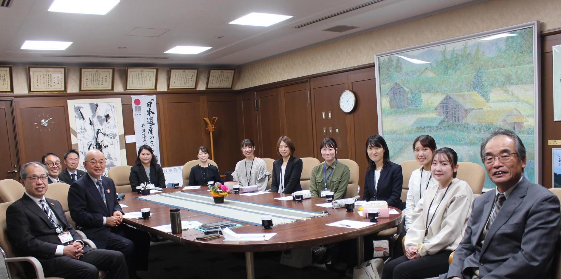 イスに座って、市の幹部職員と若手職員が記念撮影