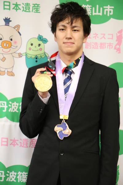 首にかけているメダルを手に取る、笑顔の溝畑 樹蘭選手の写真