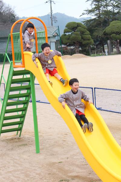 女の子が滑り台に上り男の子2人が滑り台を笑顔で滑っている写真