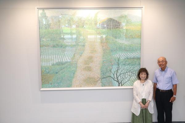 丹波篠山の農村風景(道を挟んで両側に田植えされたばかりの田園が広がっている風景の絵）をバックに中竹 毬子さんと市長が一緒に写っている写真
