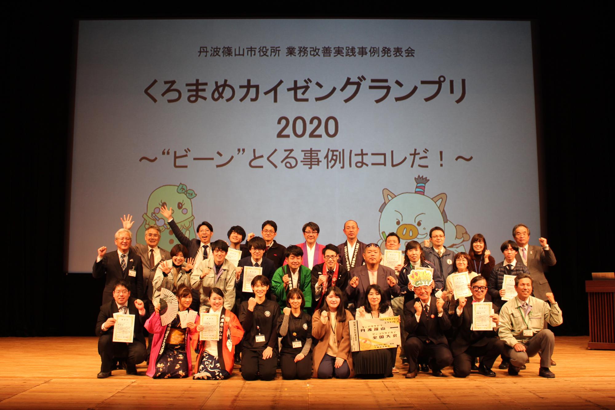 くろまめカイゼングランプリと書かれたスライドの前で撮られた発表した職員や、司会、審査員などが写っている写真