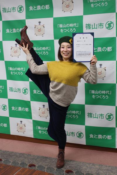 森田 まりこさんが右足を高くあげ、右手で足首を支え、左手で委任状を持ち、笑顔で写っている写真