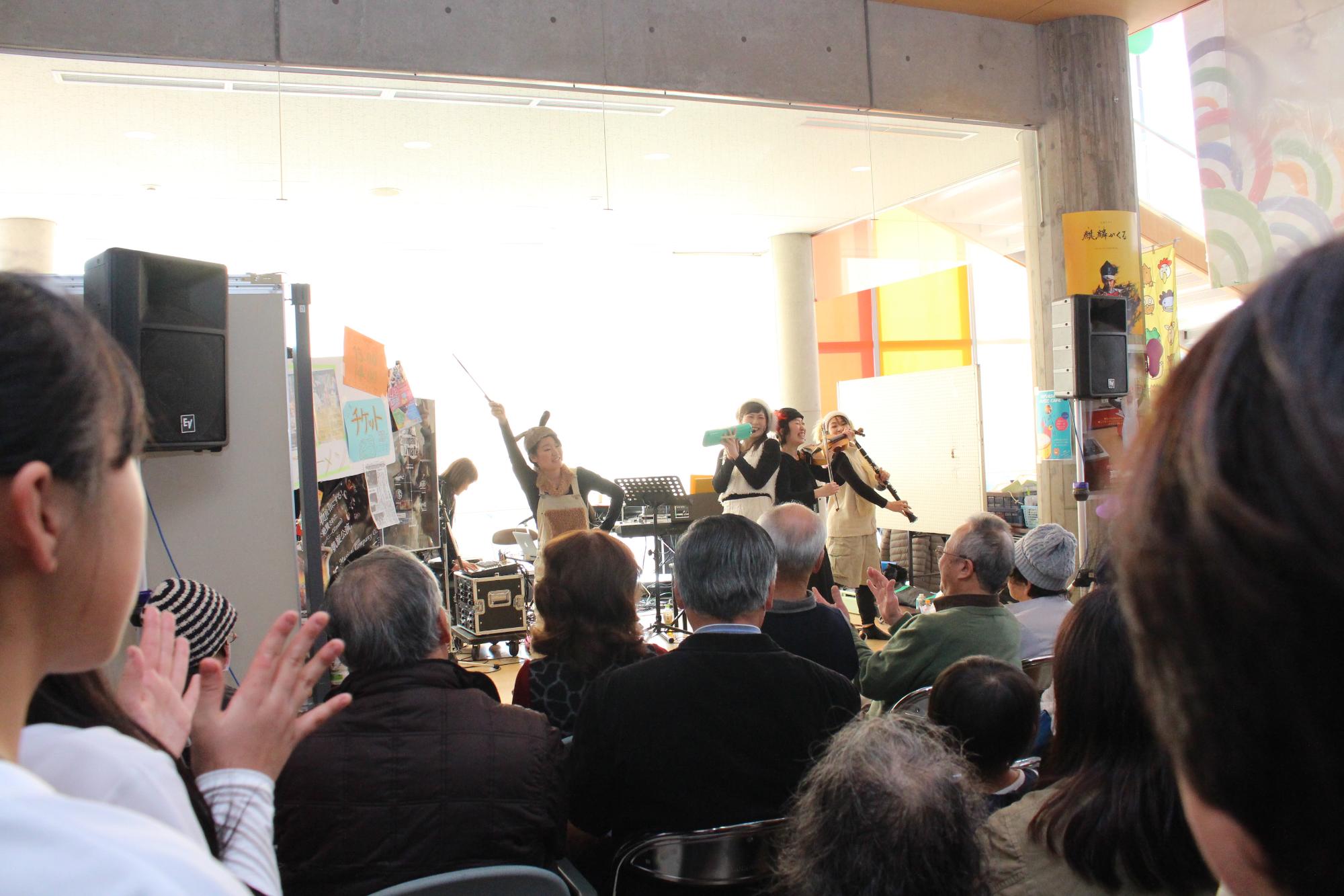 ハーモニカなどの楽器を演奏する女性のグループとそれを見ている人々の写真