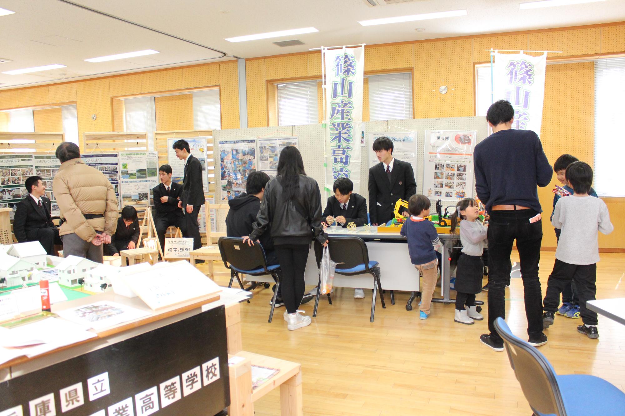 篠山産業高校のブースで説明をしたり話したりしている産業高校の生徒たちと、展示を見る人や話を聞く人や、子どもたちの写真