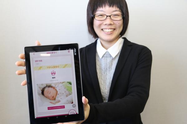 子育てアプリの画像が出ているタブレットを持っている女性の写真