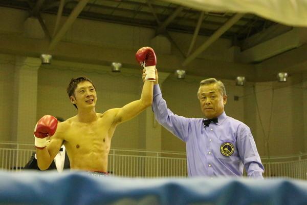 試合に勝った角谷 淳志選手の右腕を審判が持ち上げ、勝利を判定している写真