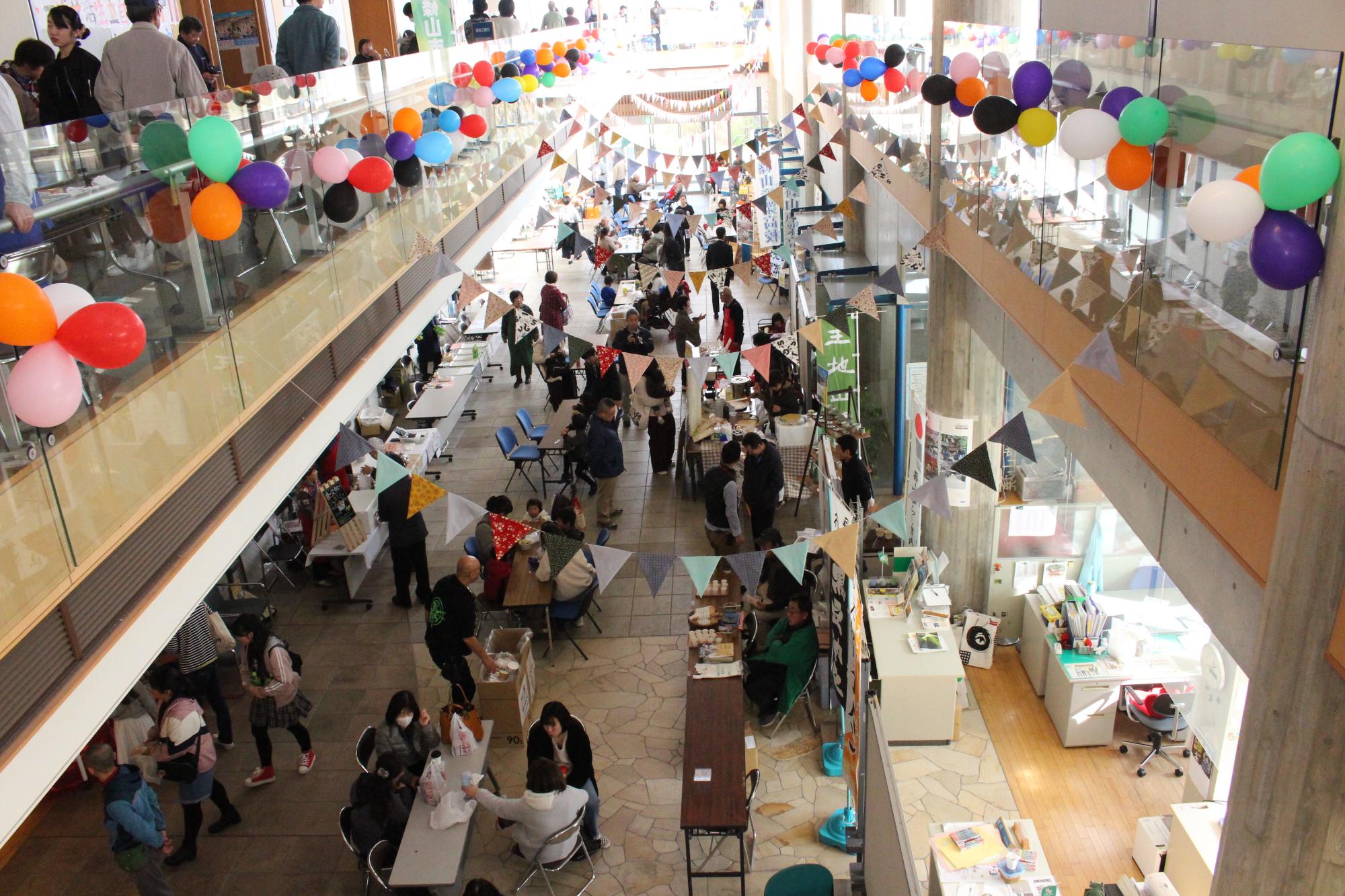 風船などが飾り付けられ、多くの人が市民センターまつりを楽しんでいる様子を2階から撮影した写真