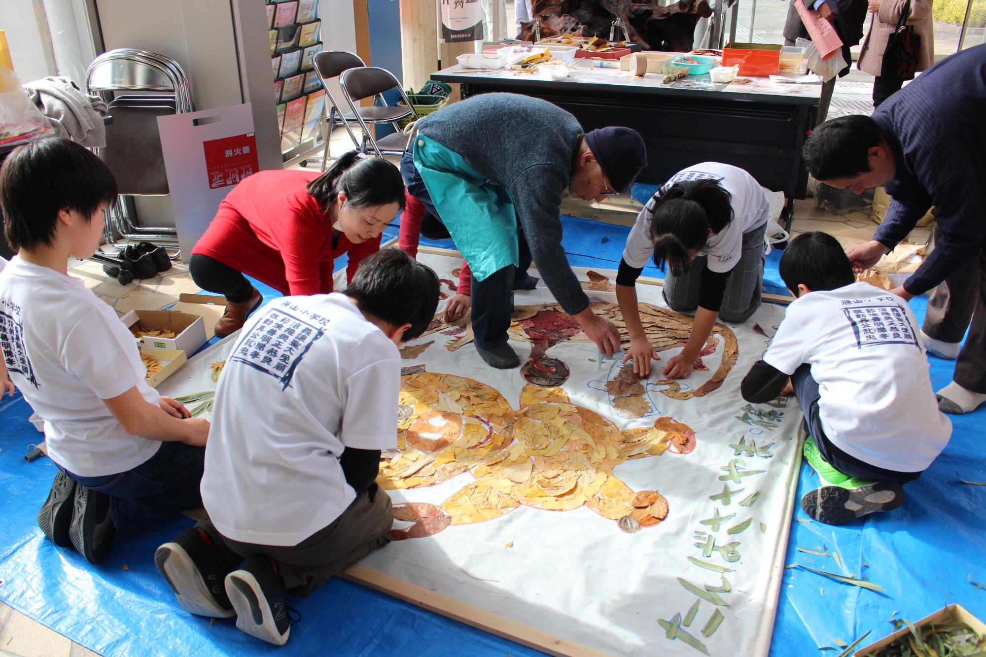 茶色の葉っぱなどを白い紙に貼って絵を作っている子どもたちなどの写真