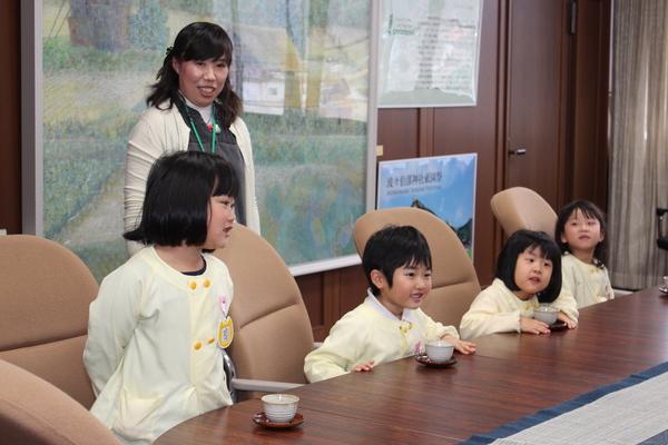 市長室の大きな椅子に園児達が座っており、テーブルには一人ずつ湯飲みに入ったお茶が出され園児の一人が立ち上がって話をしている様子の写真