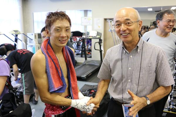 タオルを首にかけている角谷選手が市長と笑顔で握手をしている写真