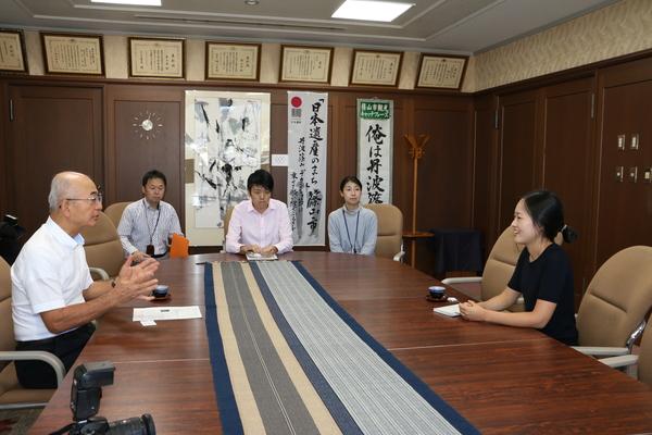 テーブルに向かい合わせに座っている酒井市長とイ・シーラさんと奥に座っている3人の市職員の写真