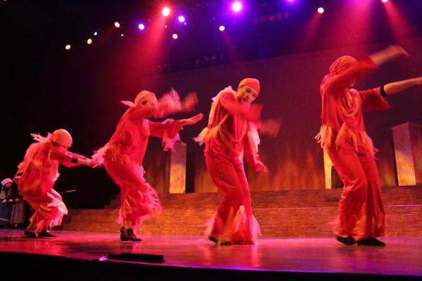 4名の出演者が両手を前に動きを表しており、その4名の方を赤赤としたライトが照らしている写真