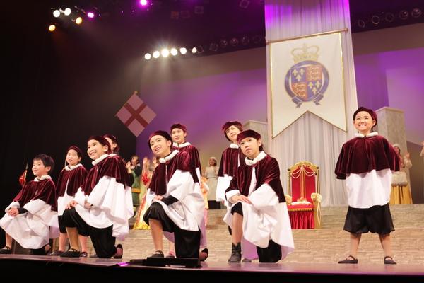 赤のベレー帽に赤白の衣装を着た子供たちが前列が右足を前に座り後ろの子供達がたちながら笑顔で遠くを眺めている様子の写真