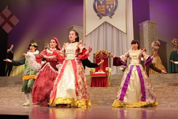 ドレスを着た女性と緑色の衣装を着た男性が歌に合わせて両手を広げ踊っている写真