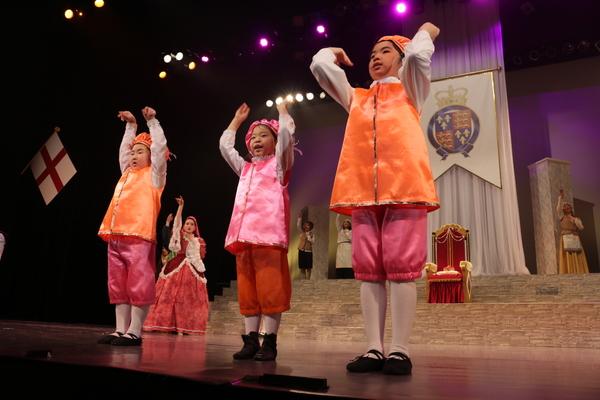 オレンジとピンクの帽子や衣装を着た子供たちが両手を上にあげている写真
