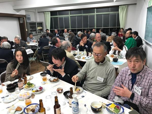 胸に名札をした人たちが机に並べられた食事をしている写真