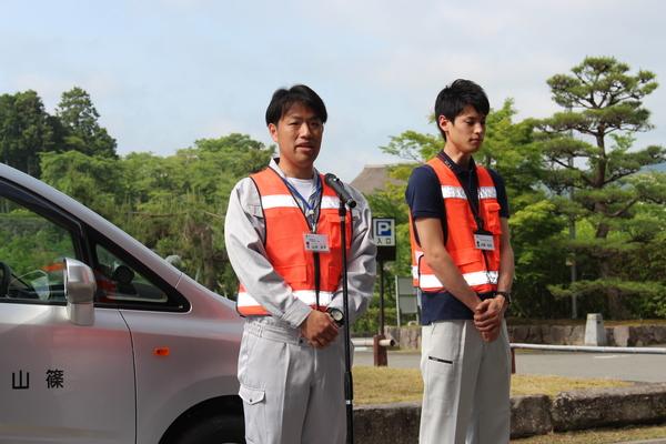 山本 圭太係長と伊藤 琢郎主事が立っており、山本 圭太係長がスタンドマイクの前で話をしている様子の写真