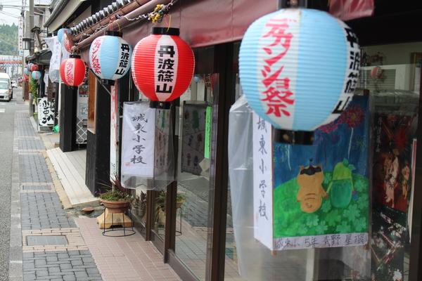 お店の前に篠山の赤と青の提灯と城東小学校の生徒の絵が描かれている灯篭が飾られている写真