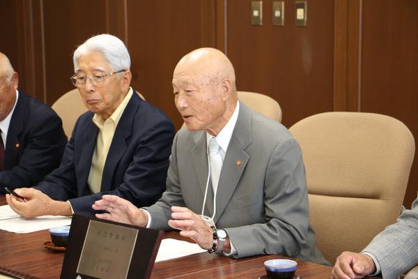 受賞者の代表が受賞の盾を前に話をしている写真