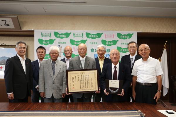 賞状と盾を持った受賞者らが市長と一緒に記念撮影している写真