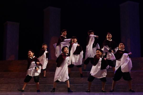 赤のベレー帽を被り、白と赤の衣装を着た子供たちが階段をつかい手を前にふりながら踊っている写真