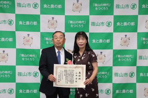 山本 清さんと妻の律子さんが一緒に表彰状を持ち記念撮影している写真