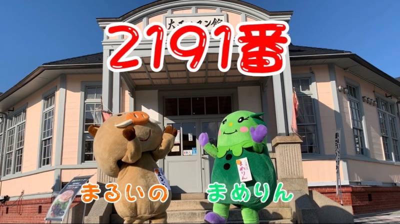 大正ロマン館前で、まるいのとまめりんが両手をあげている