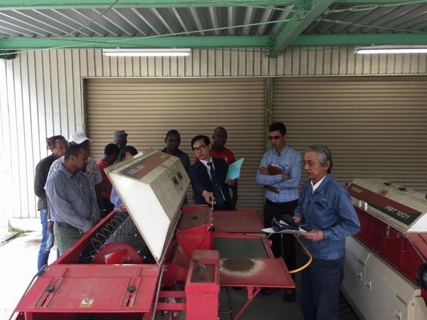 スーツを着た男性が、アフリカ、ミャンマー、インドネシア各国の農業技術職員に、農業用トラックの説明をしている写真写真