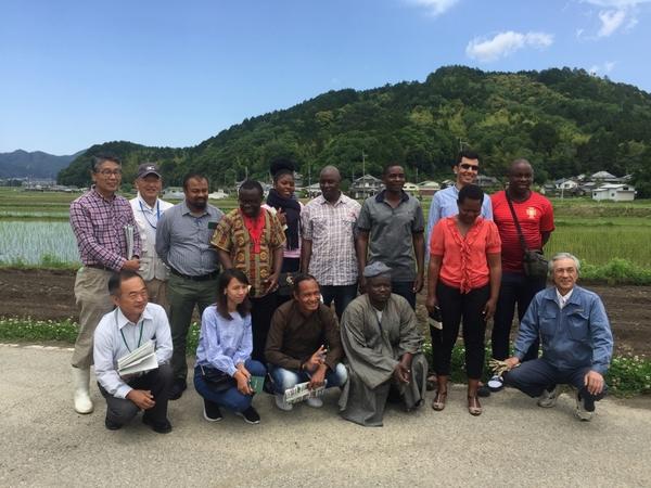 圃場の前で日本人職員男性と、アフリカ、ミャンマー、インドネシア各国の農業技術職員の集合写真
