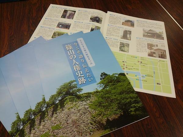 「篠山の人権史跡」の冊子が4冊扇形に並べてある下に中身を開いた1冊が長机の上に置いてある写真