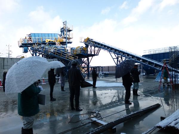 ベルトコンベア が組み立てられているような施設を傘をさして現地見学をしている様子の写真