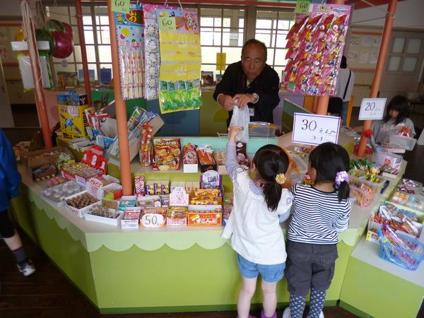 駄菓子屋さんで沢山のお菓子が並んで女の子がお菓子を買っている写真