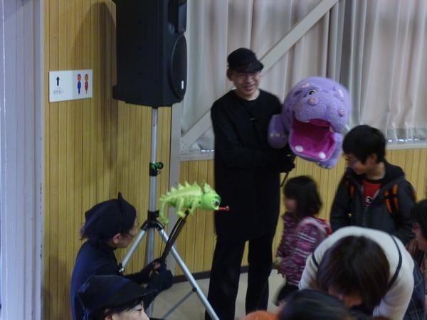黒い衣装を着た劇団員の方が子供達に人形を使って話しかけている写真