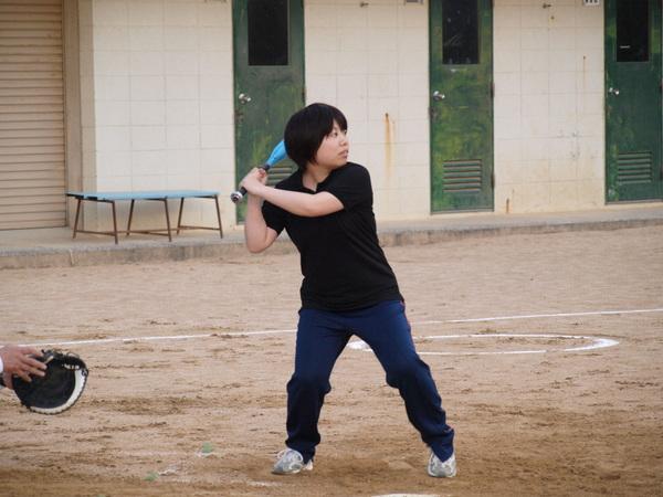 黒いティーシャツを着た岡地さんがバッターボックスに立ち、ボールを打とうとバットを両手で握り、構えている様子の写真