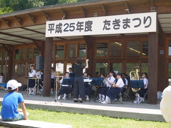 篠山東中学校の生徒が指揮者の元、楽器を演奏している様子を青いシャツを着た子供が聞いている写真