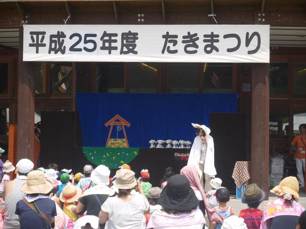 舞台が作られ、女性が人形劇をしているところを親子で一生懸命見ている写真