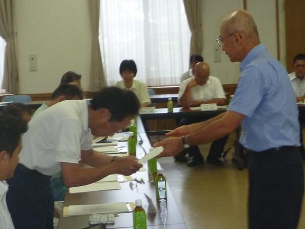 メガネをかけた男性が頭を下げて両手で用紙のような物を、市長より受け取っている様子の写真