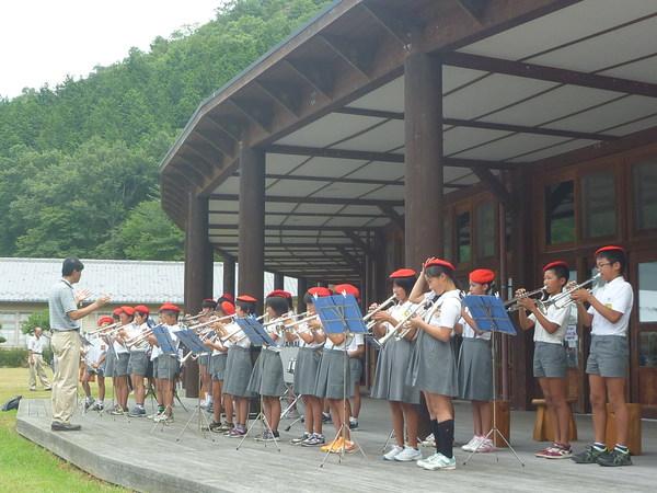 制服を着て赤いベレー帽姿の子供達が起立して、トランペットを弾いている写真