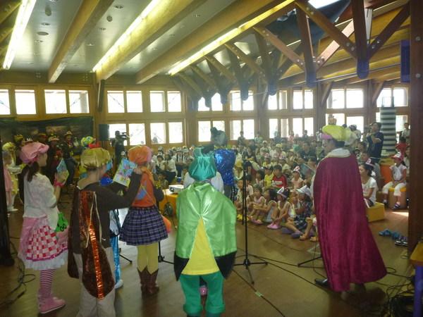 手作りの服を着て劇をしている子供達の後ろから観客席の大人や子供を写した写真