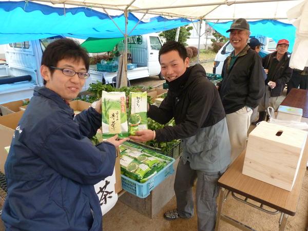 販売ブースで笑顔の男性2名が製品のお茶を持っている写真