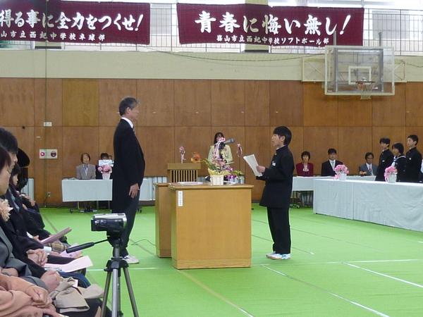 演台に立っている礼服を着た男性を前に代表の生徒が式辞を述べている写真