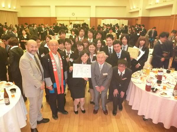 懇親会の会場にて、中央大学 細野ゼミの参加者が集まり1名が賞状を広げて見せ、市長と一緒に写っており、会場には沢山の人で賑わっている様子の写真