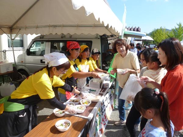 テントの下でじょうとうまるごと丼を準備している女性と、買いに来た女性客の写真