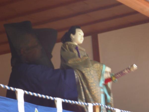 黒子さんが、刀を持つ人形を持っている写真