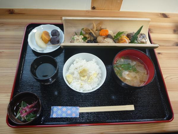 栗ご飯、みそ汁、漬物、梨・柿・葡萄、竹を縦半分に切り出来た竹の器に盛られた煮つけが乗ったお膳の写真