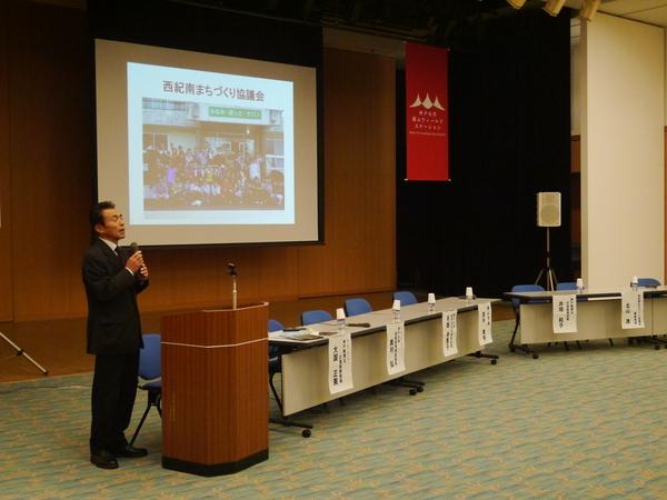 西紀南まちづくり協議会の北山事務局長が、スライドの斜め左あたりに立ち、マイクを持って話をしている写真