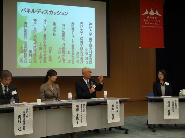 パネルディスカッションというスライドの前で、篠山市長がマイクを持ち話をしており、神戸大学と神戸新聞社の方合わせて4人が写っている写真