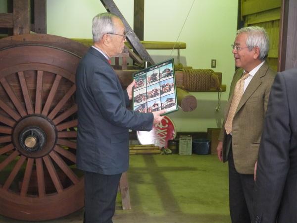 木でできた大きな車輪の前で文化庁長官が説明を聞いている写真