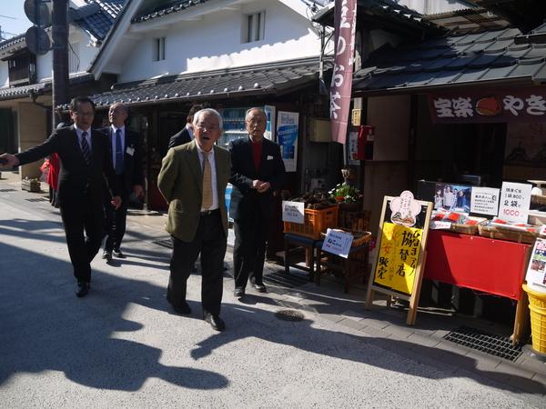 宝落やきと書かれたお菓子屋の前の道路を職員の説明を聞きながら文化庁長官が歩いている写真
