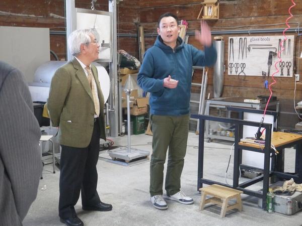 ハサミなどの工具のあるガラス工房を職員の説明を聞きながら見学する文化庁長官の写真